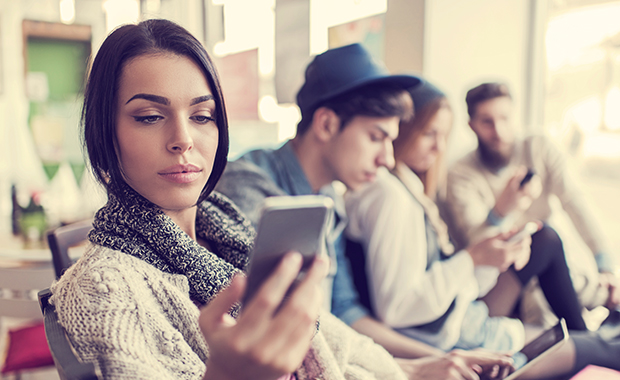 Young woman with annoyed expression looks at phone while friends sit in background