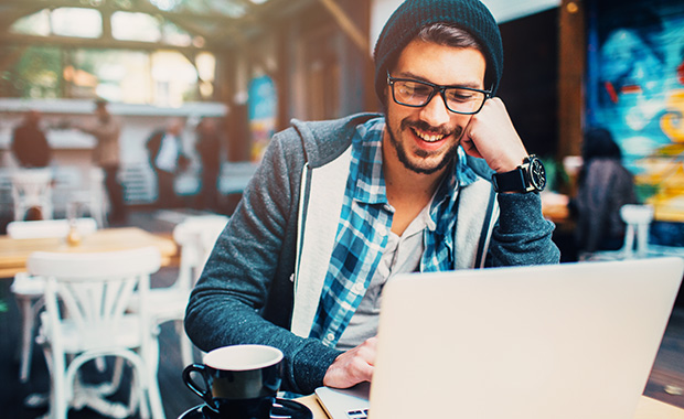 Smiling man reads from laptop in café 