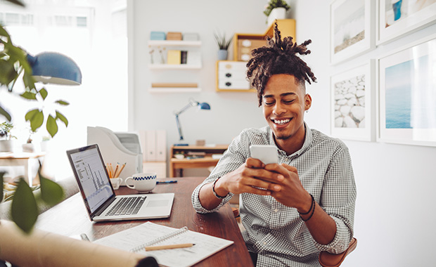 Smiling young man sitting at desk looking at smartphone