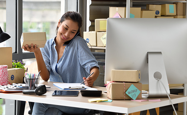 Woman sits at desk behind computer holding package