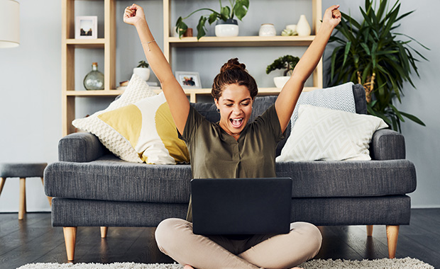 Woman sitting on floor with laptop raises arms victoriously