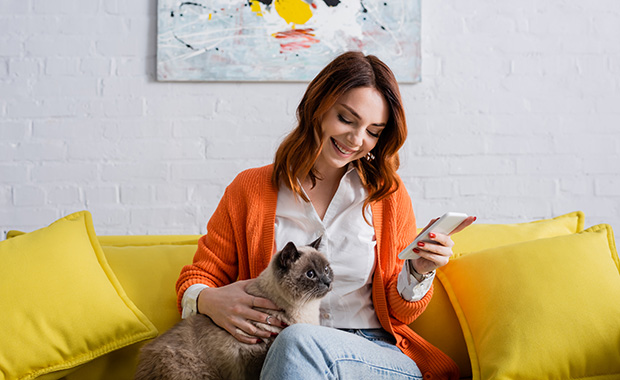 Smiling woman with cat on lap looks at smartphone