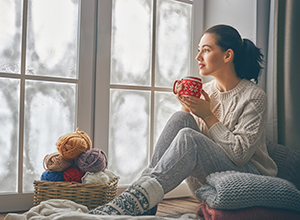 Woman holding cup looks out frosty window
