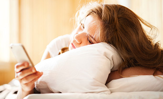Sleepy woman lying in bed looking at phone