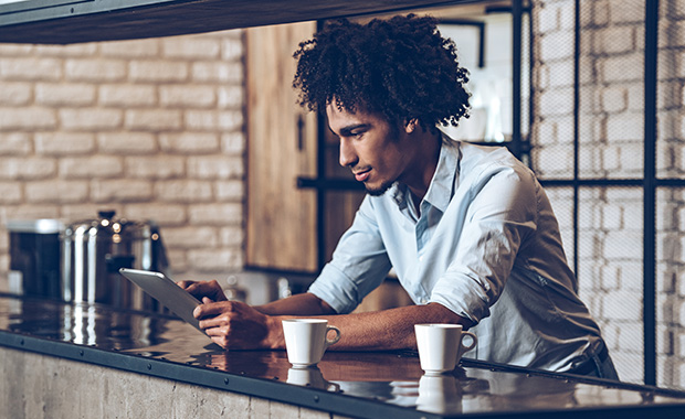 Man stands at counter in café looking at tablet computer