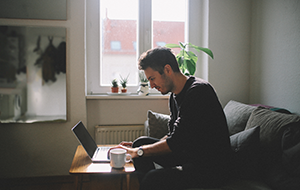 Side view of a man sitting in a living room looking at a laptop on a coffee table.