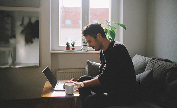 Side view of a man sitting in a living room looking at a laptop on a coffee table.