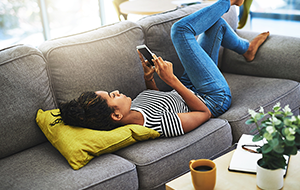 Young woman lies on couch looking at iPhone