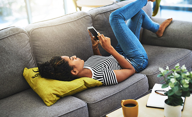 Young woman lies on couch looking at iPhone