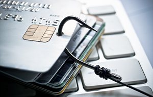 A fishhook piercing several credit cards placed on a computer keyboard.