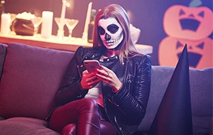 Woman in skull mask looks at smartphone at a Halloween party