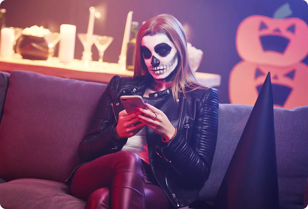 Woman in skull mask looks at smartphone at a Halloween party