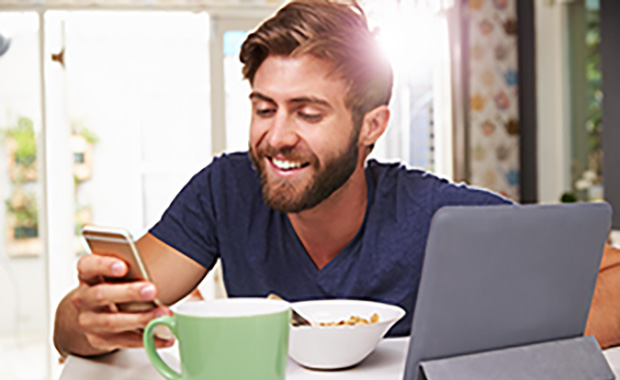Man eating breakfast while using digital tablet and phone