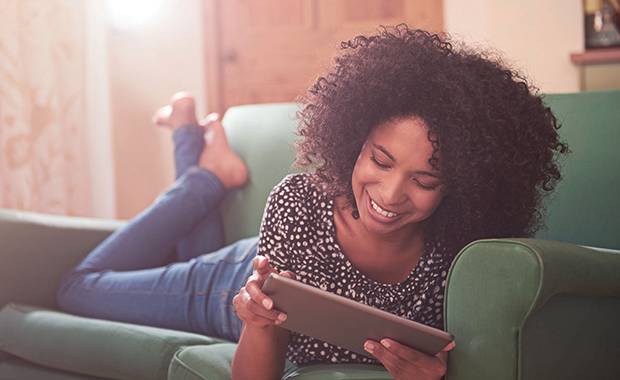 Smiling woman lying on couch reading from iPad