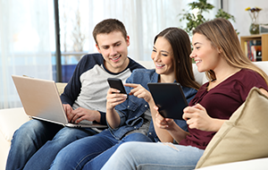 Smiling young man and two young women sit on couch looking at phone held by woman in the middle