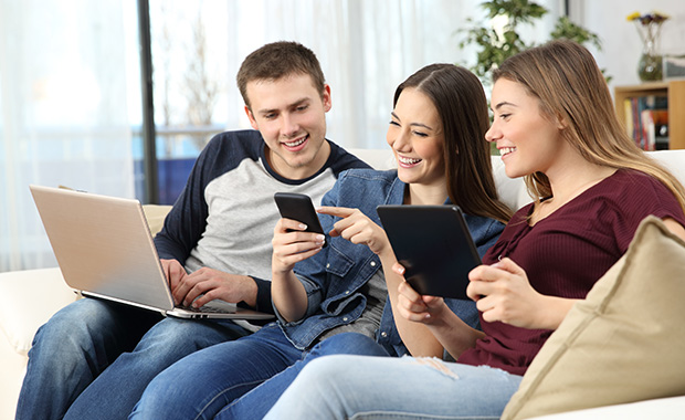 Smiling young woman and senior man sit in front of laptop looking at phone