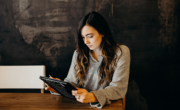 Woman sits in dark café looking at tablet with concerned expression