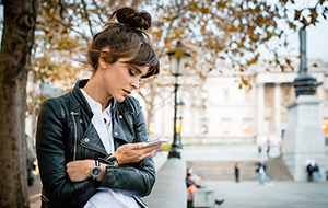 Woman sits outdoors looking at smartphone with serious expression