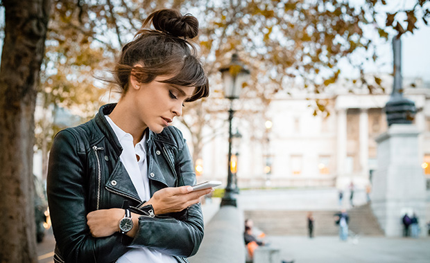 Woman sits outdoors looking at smartphone with serious expression