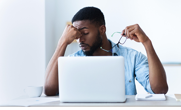 Man holds glasses and rubs eyes while working at laptop