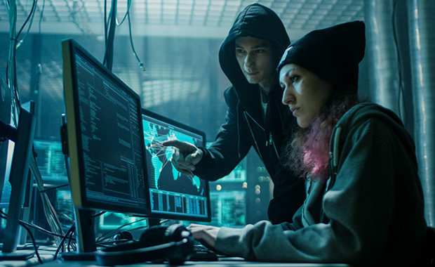 Two women dressed in black in dark warehouse room working on computer with two screens