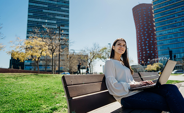 Professional woman sits on bench smiling and holding laptop