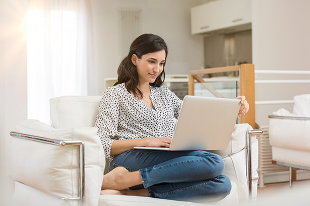 Woman with laptop on lap sits in armchair and read screen with interested expression