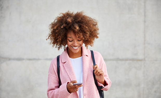 Woman in pink jacket looks at smartphone and smiles