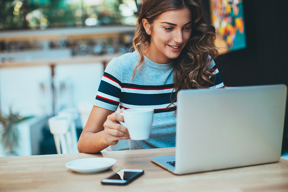 Young woman in cafe reading blog on laptop