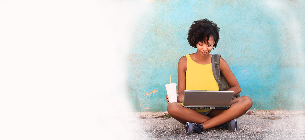 Smiling woman with laptop sitting cross-legged in front of blue wall