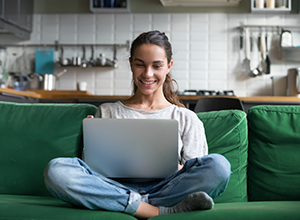 Smiling young woman on couch holding laptop