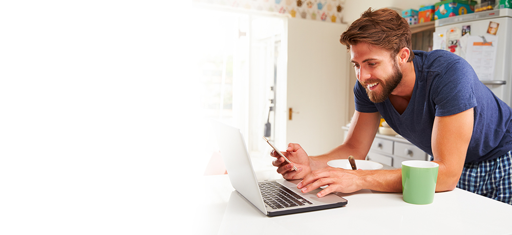 smiling man using smartphone and laptop activating 2fa
