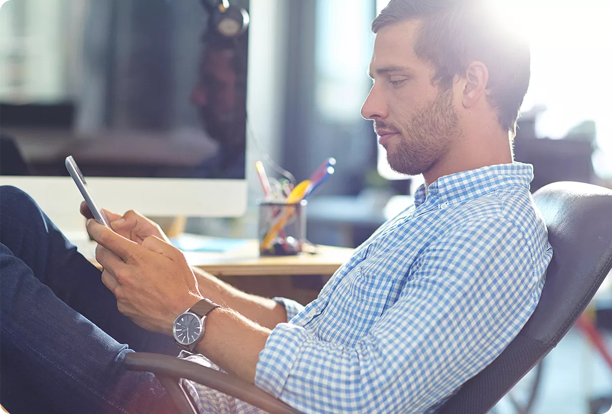 Ein Mann sitzt in einem Bürostuhl und bedient ein Smartphone.