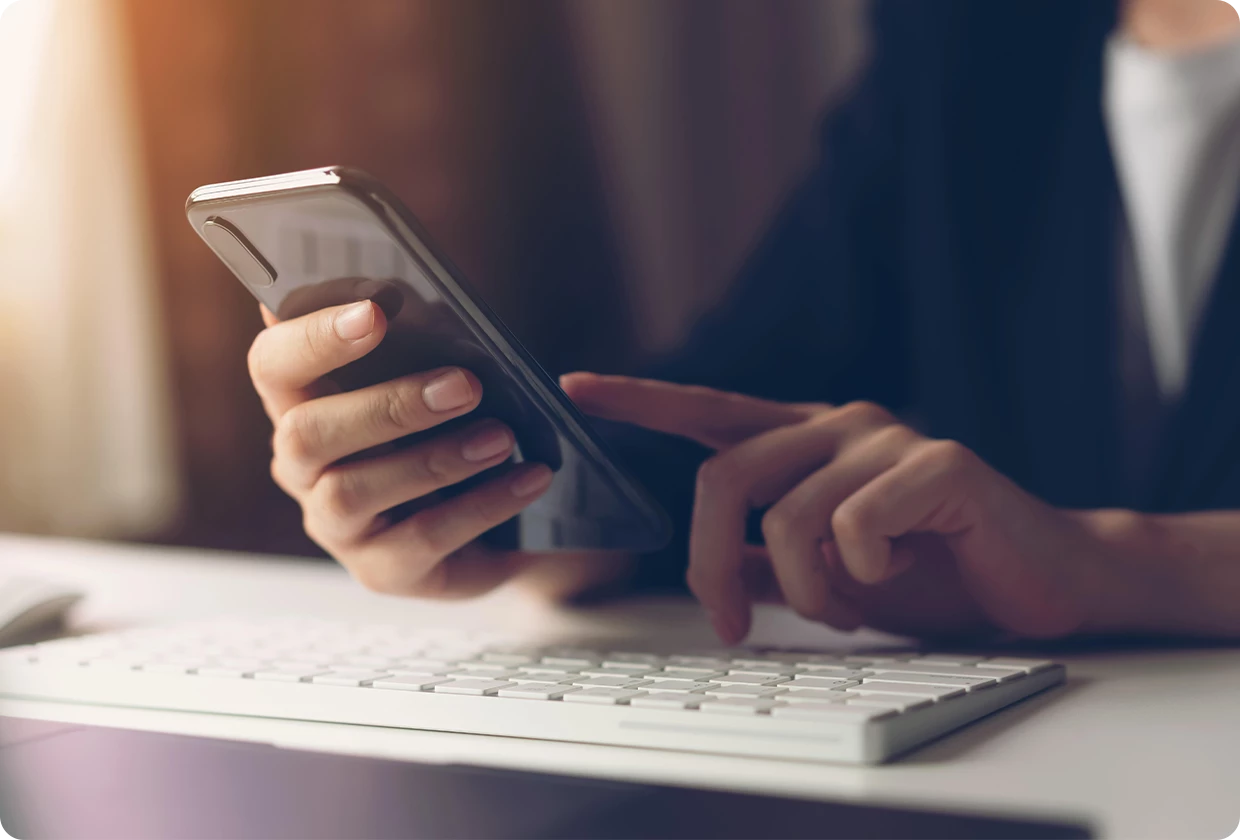 Person vor geöffnetem Laptop, die ein Handy in der Hand hält
