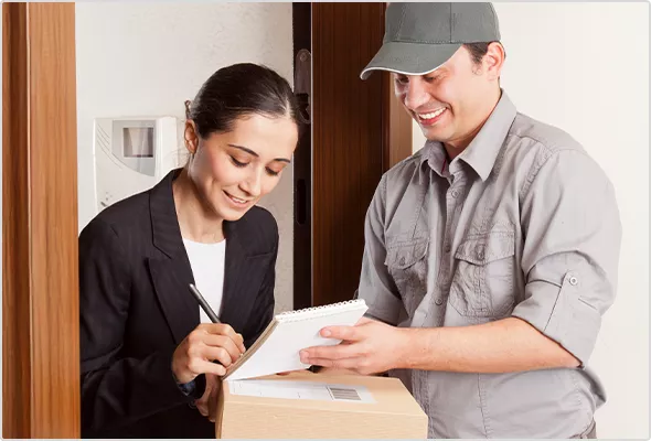 Eine Frau nimmt an der Türschwelle lächelnd ein Paket von einem Zusteller entgegen.