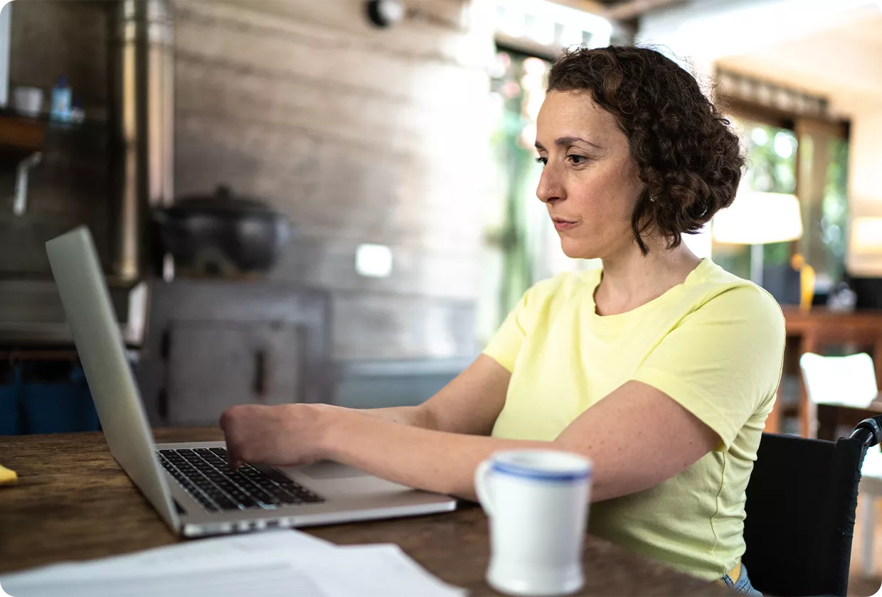 Frau mit einer sichtbaren Handbehinderung tippt am Laptop.