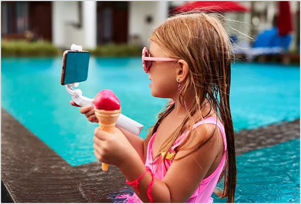 Szene am Pool: Kleines Mädchen mit rosa Bikini und Eis in der Hand filmt sich mit Selfiestick