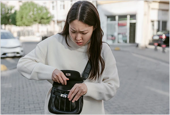 Junge Frau, die skeptisch in ihre Handtasche schaut.