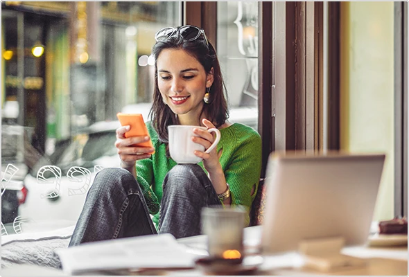 Eine junge Frau sitzt im Café und schaut entspannt auf ihr Handy.