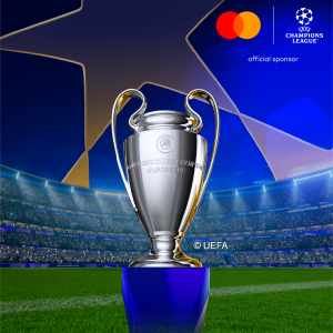 Silberner UEFA Champions League Pokal auf blauem Sockel vor einem vollbesetzten Stadion mit blauem Nachthimmel, Mastercard- und Champions-League-Logos oben rechts.