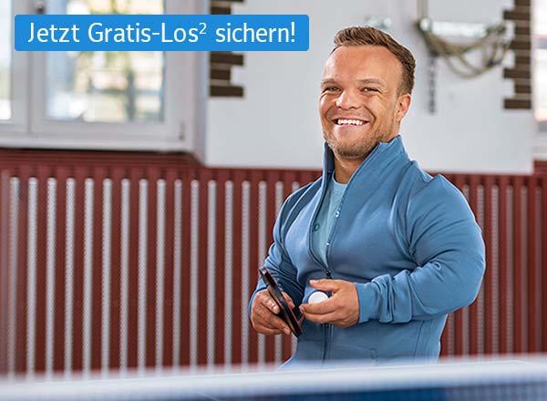 Lächelnder Mann in blauem Sportjacke hält Tischtennisschläger und Ball in einer Halle