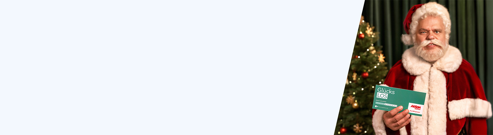 Weihnachtsmann in rotem Kostüm mit weißem Pelzbesatz hält eine grüne Karte vor einem geschmückten Weihnachtsbaum.