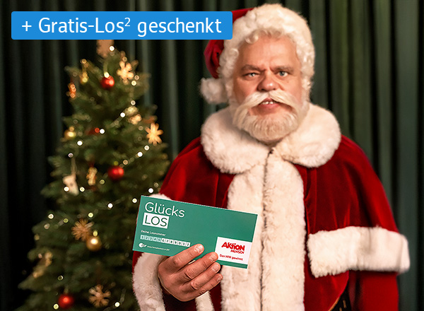 Person in rotem Weihnachtsmannkostüm hält ein grünes Los mit der Aufschrift 'Glücks LOS' vor einem geschmückten Weihnachtsbaum.