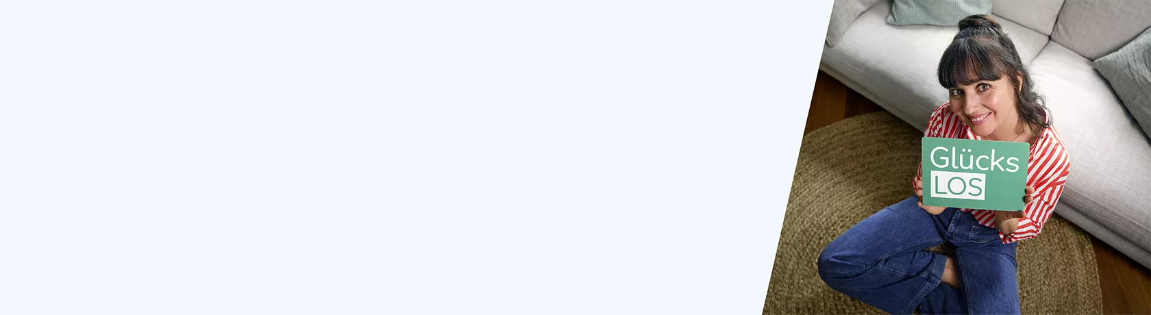 Frau mit rot-weiß gestreiftem Hemd hält rotes Smartphone vor sich, sitzt an Holztisch vor Bücherregal und Fenster mit Blick ins Grüne.