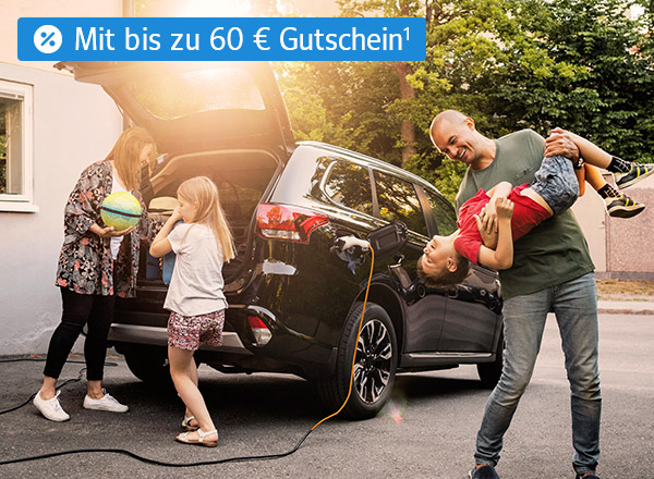 Ein Auto mit geöffnetem Kofferraum steht vor einem Haus. Eine Familie steht vor dem Auto. Die Mutter lädt Gepäck in den Kofferraum, ein Kind steht daneben. Der Vater steht scherzend mit einem weiteren Kind neben dem Fahrzeug.