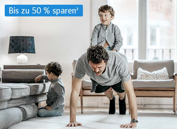 Ein Mann macht Liegestütze im Wohnzimmer, während ein Kind in der Nähe spielt uns eines auf seinem Rücken sitzt, oben links in der Ecke ist der hinweis geschrieben, dass man jetzt bei Cosmos Direkt 50 % sparen kann auf die Unfallversicherung²