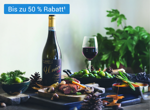 Flasche Rotwein mit goldener Kapsel und schwarzem Etikett 'Unico', daneben Weinglas mit Rotwein, grüne Trauben und Tannenzapfen auf Tisch.