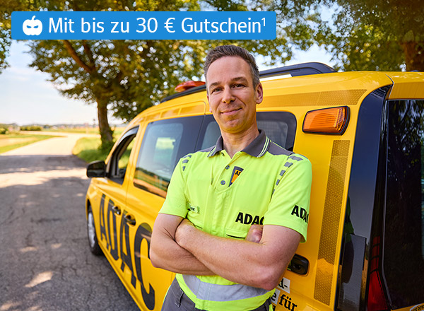 ADAC-Mitarbeiter in gelbem Polo steht vor gelbem Pannenhilfsfahrzeug auf Landstraße, Text 'Mit bis zu 30 € Gutschein'