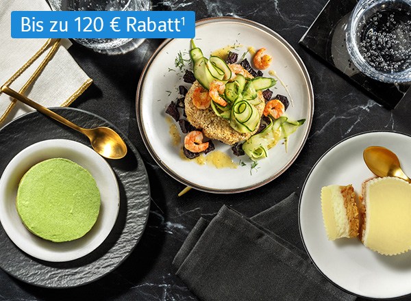 Teller mit Garnelen, Desserts und Besteck auf dunklem Tisch, bis zu 120 € Rabatt.