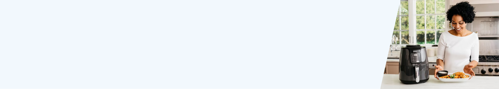 Frau in weißem Oberteil steht in moderner Küche vor schwarzer Heißluftfritteuse und hält Teller mit frittiertem Essen und Dip-Schale.